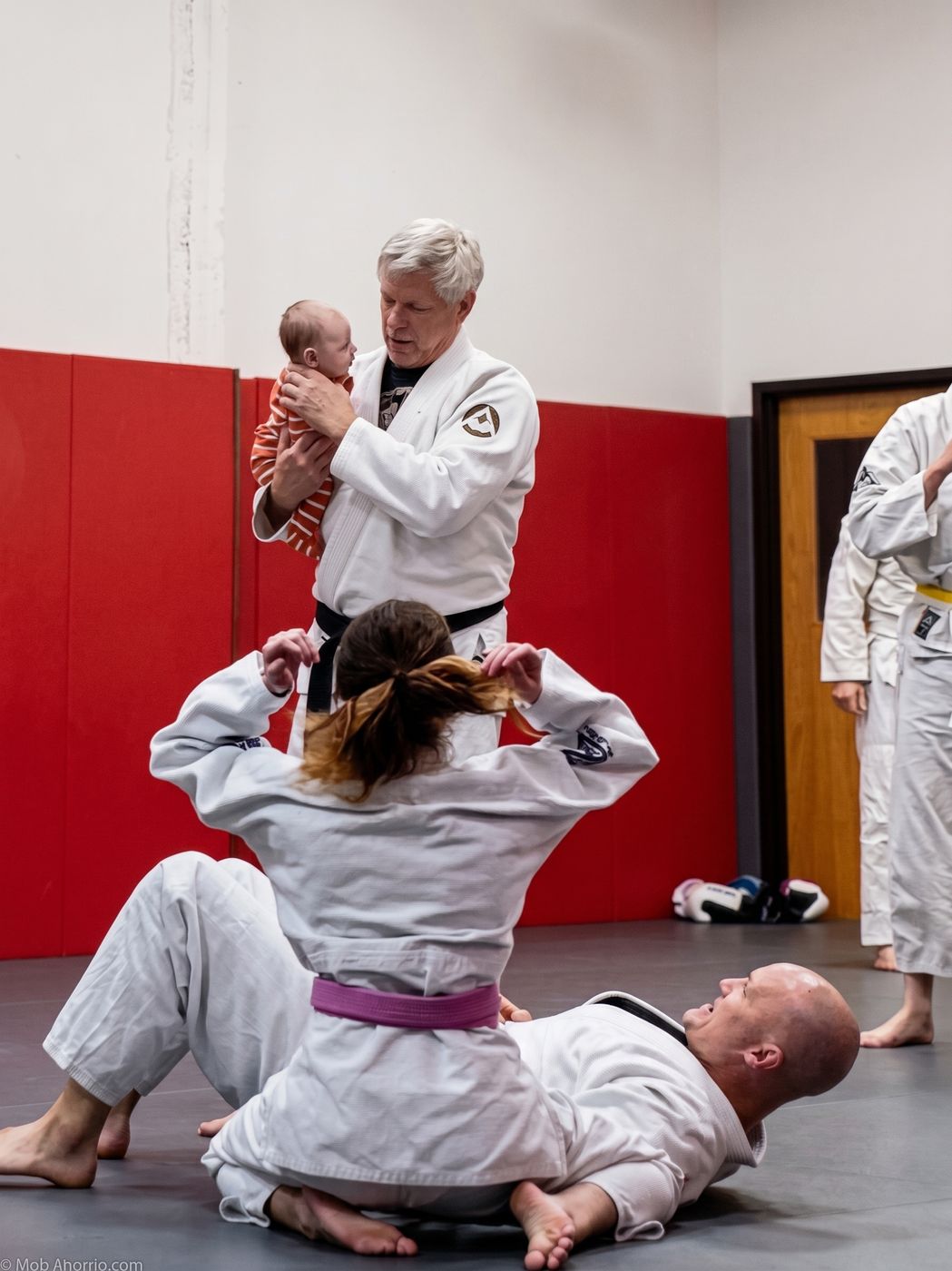 Master Dave Niska holding his grandson while Jiu-Jitsu students train at Invictus